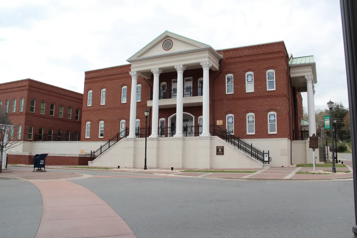 The red-brick Gilmer County courthouse with its white columned portico and clock tower, photographed from the square on a sunny day with trees in leaf.